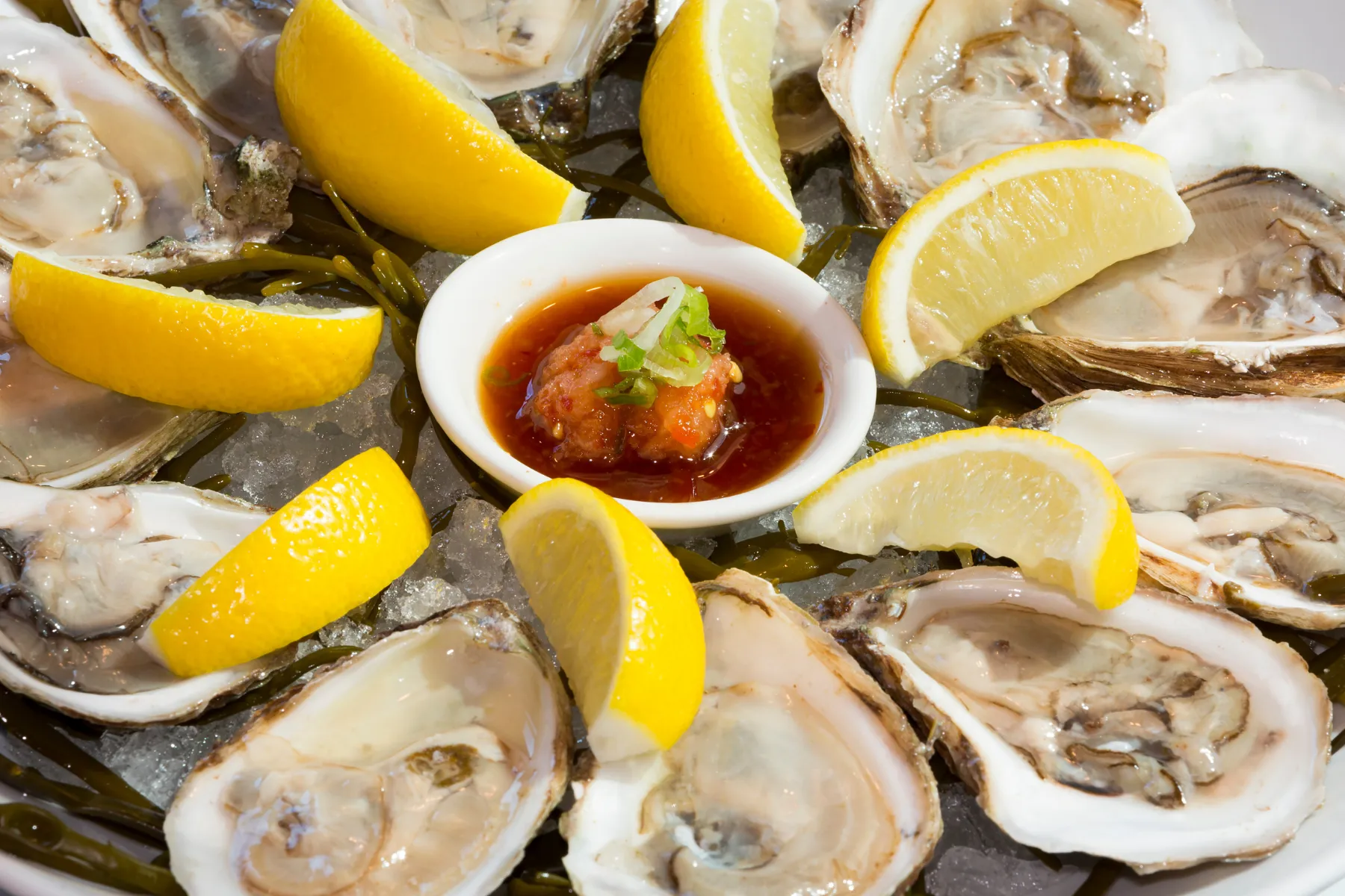 Fresh oysters on ice with lemon wedges and a small bowl of cocktail sauce.