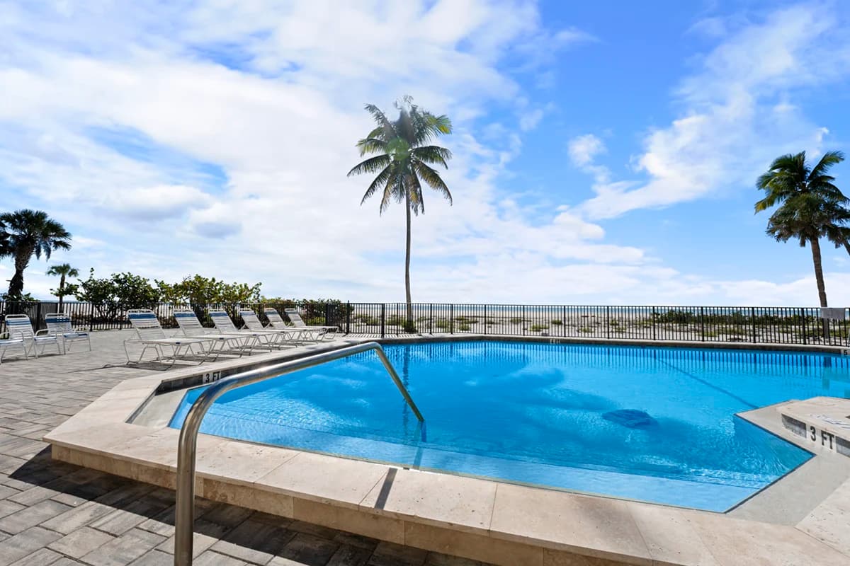 Poolside view with palm trees and ocean backdrop on a sunny day